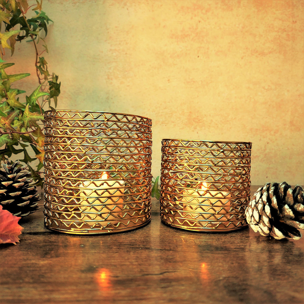 Two wire mesh metal candleholders, one big and one small, in gold finish with lit candles