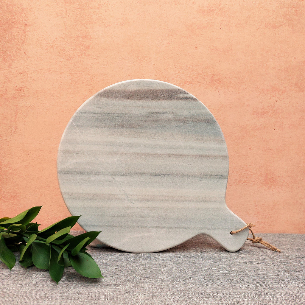 a Megha Round Marble Cheese / Chopping Board on a table next to a plant.