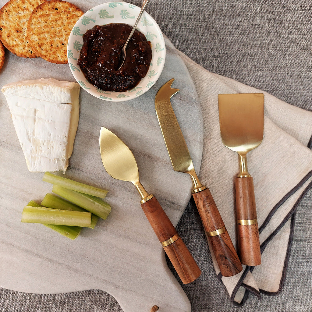 a wooden cutting board with the Kath Cheese Knives Set with Gold Blade and Wood Handle, celery and crackers.
