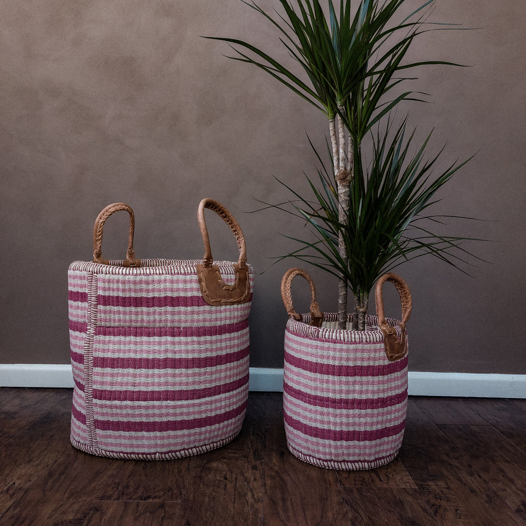 Two Gulabi Striped Pink Cotton & Jute Handloom Baskets next to a plant.