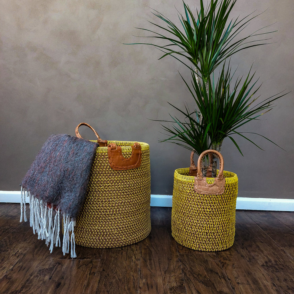 two Manjal Jute and Cotton Coil Baskets on a wooden floor next to a plant.